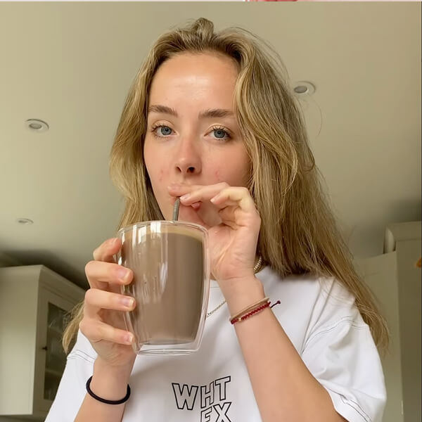 Person drinking a beverage from a glass with a straw in a kitchen